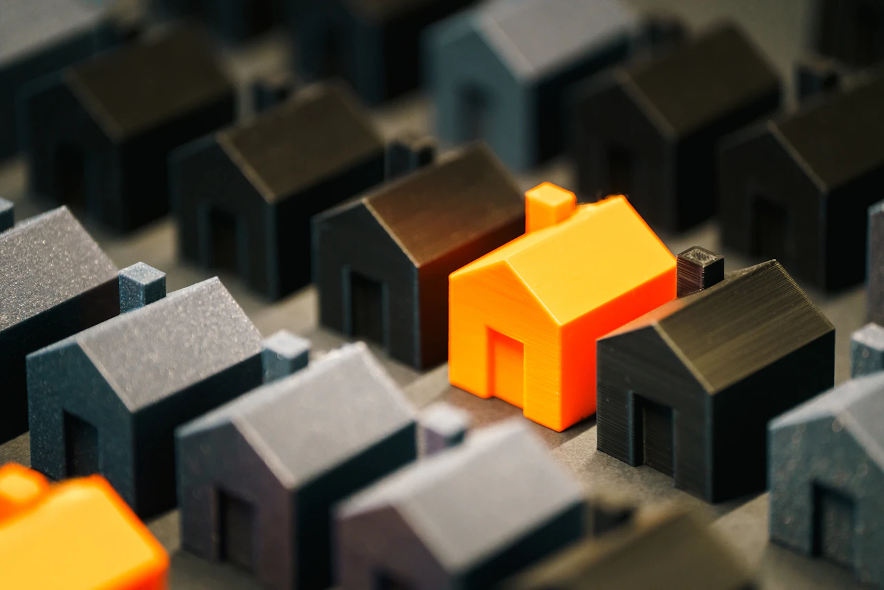 Ein orangefarbenes Modellhaus zwischen vielen grauen – Symbolbild für die große Auswahl der Käufer