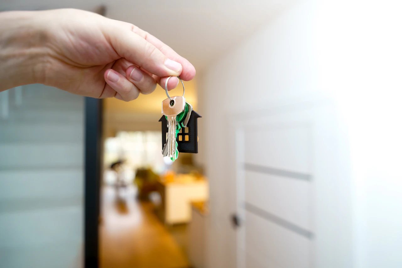 Hand hält einen Hausschlüssel mit Haus-Anhänger an der offenen Wohnungstür – Symbolbild für die Übergabe des Elternhauses