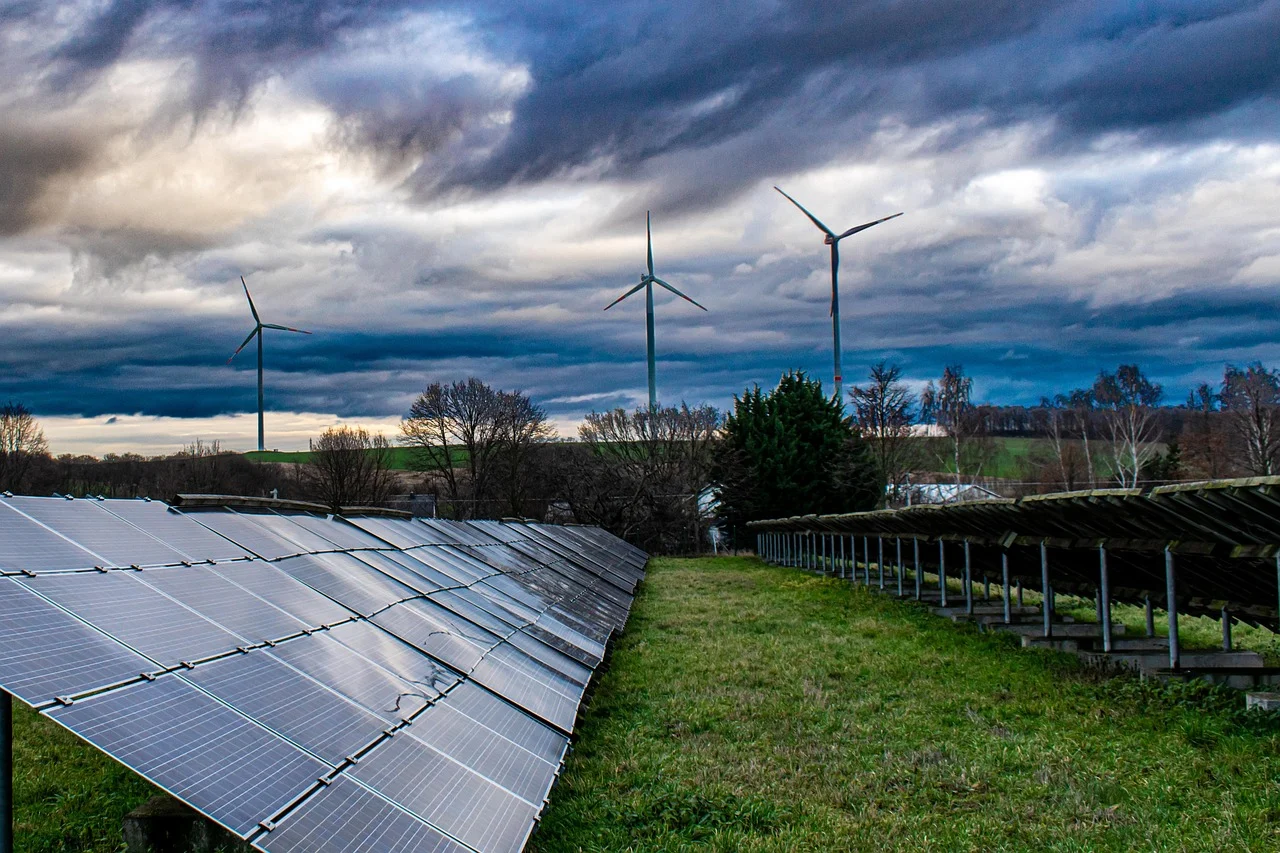 Solarpark mit Windrädern im Hintergrund unter bewölktem Himmel