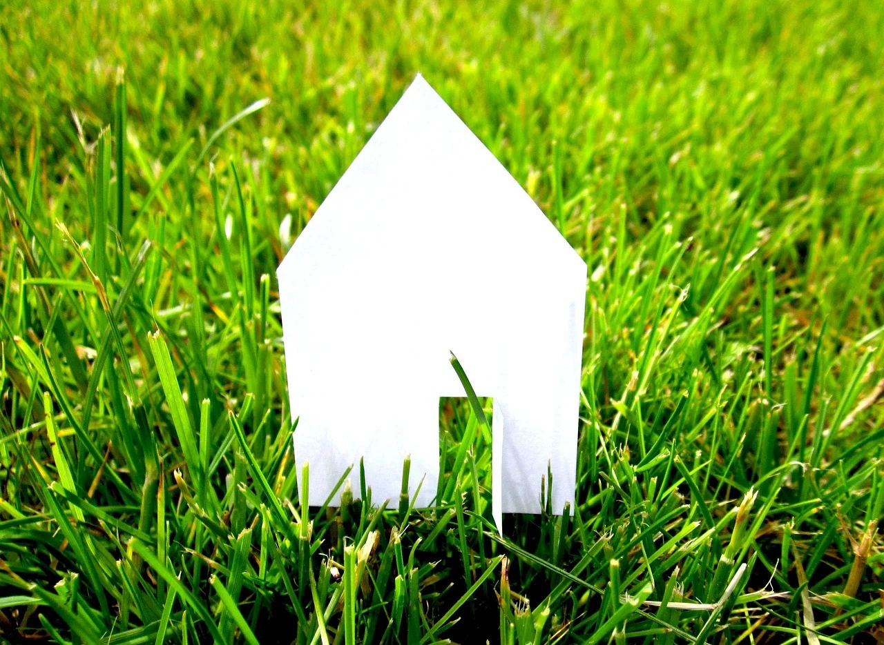 Weißes Haus-Symbol aus Papier im grünen Gras – Symbolbild für Wohneigentum